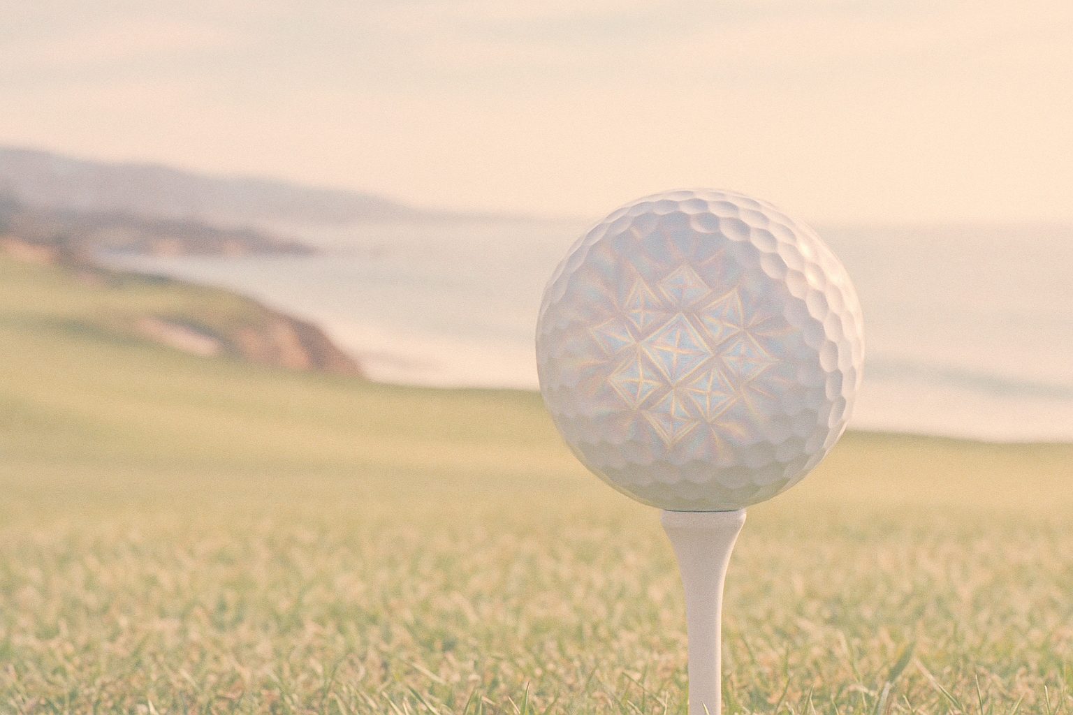golf ball on a tee, washed out filter with fractals where the light reflects. oceanside golf course in the background